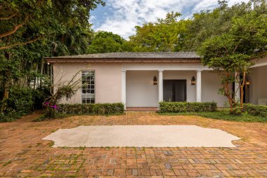 Sıcak renklerde ev cephesi, kaldırım kaldırımı, tropik bitki örtüsü, mavi gökyüzü.