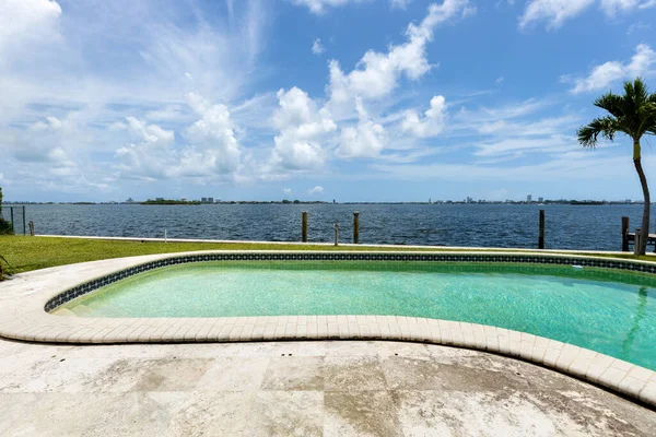 Patio with pool, wooden party wall, tropical plants , waterfront and blue sky, sky urban in background in the neighborhood of miami shores