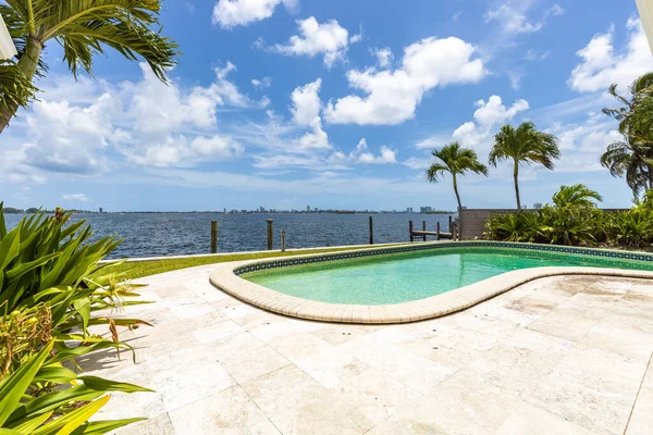 Patio with pool, wooden party wall, tropical plants , waterfront and blue sky, sky urban in background in the neighborhood of miami shores