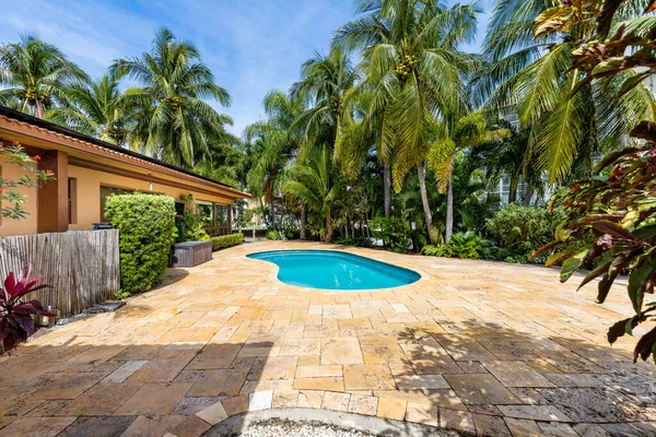 Beautiful backyard with pool of a property in Miami Bay, palm trees, shrubs, tropical plants, cobblestone floor, blue sky