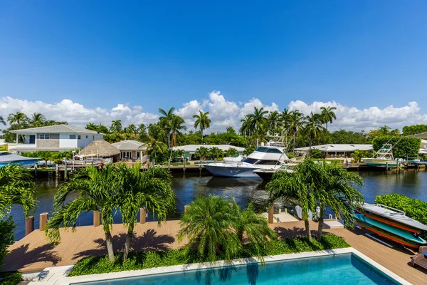 View from balcony to canal with boats in Miami neighborhood, with abundant vegetation, palms and tropical plants, swimming pool, white railing