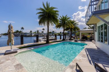 Barselona Kanalı 'na bakan modern lüks evin arka bahçesi Fort Lauderdale, Miami' de, güneşli havuz, açık koltuklar, fayans zemin.