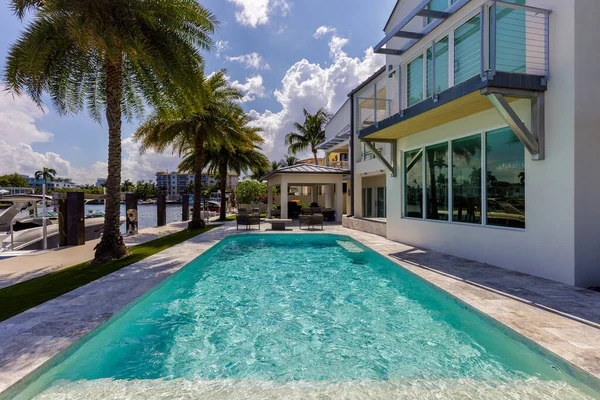 Backyard of modern luxury house facing the barcelona canal river, in fort lauderdale, miami, swimming pool with sun loungers, outdoor armchairs, tile floor
