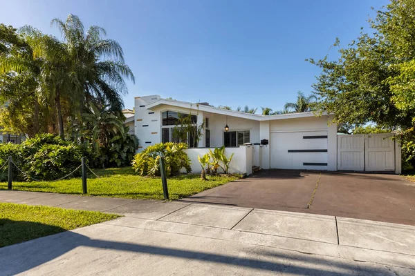 stock image White modern house facade, with driveway, garage, front yard, short lawn, palms, tropical plants, cloudless blue sky