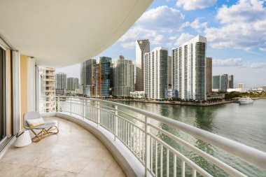 View from balcony on Brickell Key island in Miami, modern buildings and towers, boats, bridges, sea, outdoor chairs, white railing clipart