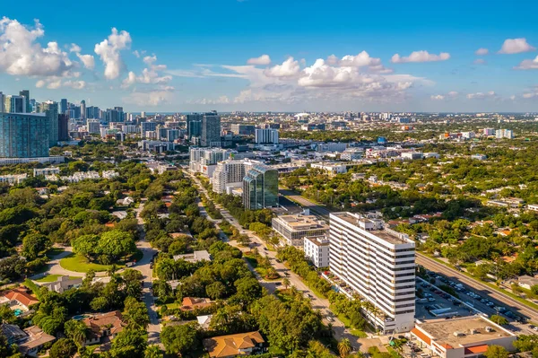 Aerial view of urban area in neighborhood with Biscayne Bay view, modern buildings, towers, summer weather, streets with cars, lush tropical vegetation around, blue sky with clouds