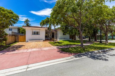 Köşedeki evin ön cephesi ağaçlarla çevrili ve park yeri olan palmiye ağaçları, kısa çimenler, fayans çatısı, mavi gökyüzü