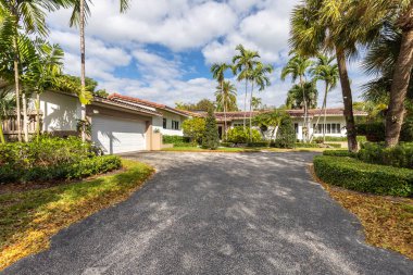 Koloni tarzı ev cephesi, kırmızı fayanslarla çevrili, tropikal bitki örtüsü, garaj yolu ve ön kapıya giden yol, mavi gökyüzü