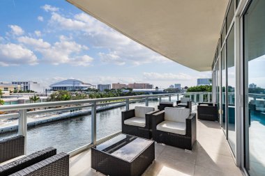 Miami 'nin Spring Garden mahallesindeki bir balkondan, Miami Nehri' ne bakan, turkuaz renkli camlı alüminyum parmaklıklar, dış mobilyalar, koltuklar. ve masalar, inşaat alanları, modern binalar, mavi gökyüzü