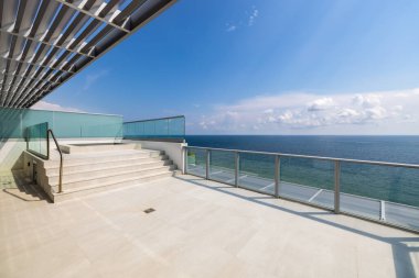 Fort Lauderdale plajına doğru kaplıcayla balkondan manzara, turkuaz camlı alüminyum bant, mavi gökyüzü, güneş pansiyonları.