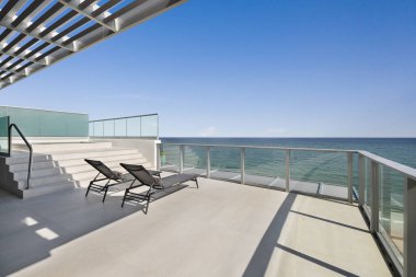 Fort Lauderdale plajına doğru kaplıcayla balkondan manzara, turkuaz camlı alüminyum bant, mavi gökyüzü, güneş pansiyonları.