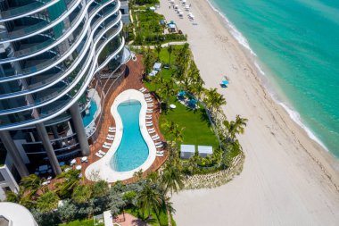 Modern kuleleri, plajı, koyu mavi gökyüzü, arka planda bulutlar, şehir manzarası, yüzme havuzları, turkuaz deniz ile Sunny Isles Beach sahil şeridinin insansız hava aracı görüntüleri.