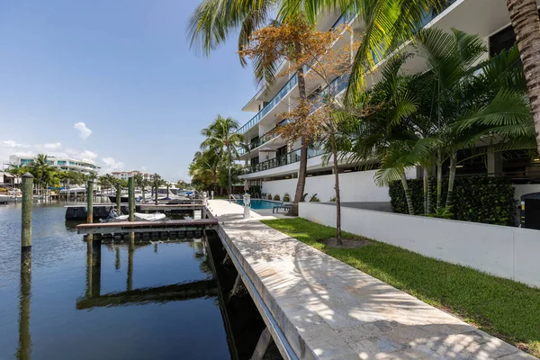 View from the pier in the Nurmi Isles neighborhood in Fort Lauderdale, canals with boats everywhere, swimming pool, sun loungers, houses and modern buildings, tropical climate with palms, bushes, trees, blue sky and skyline on the sea
