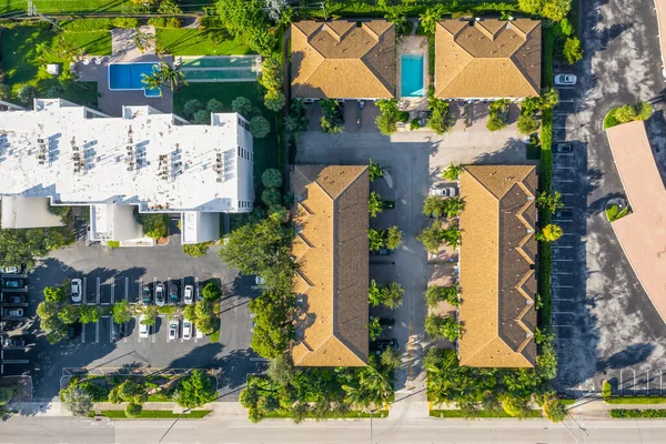 Aerial drone shot of suburban neighborhood in Pompano Beach, with bushes, trees, tiled roofs, parking areas, palms, trees, canals.