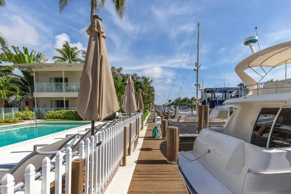 Viewpoint of wooden decked dock, with lots of parked boats, short grass, lush tropical vegetation, palms, bushes, blue sky, in the Nurmi Isles neighborhood, Fort Lauderdale, Florida