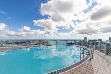 Point of view of circular pool on terrace of building in Downtown Miami, with spectacular modern and luxurious buildings and towers, streets with cars, sea in the background with blue and imposing sky