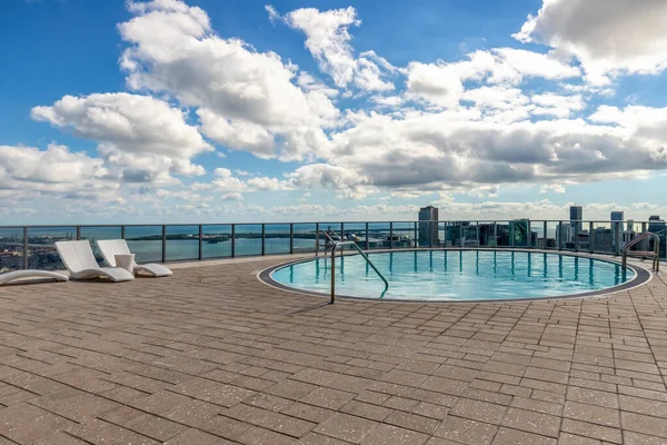 Point of view of circular pool on terrace of building in Downtown Miami, with spectacular modern and luxurious buildings and towers, streets with cars, sea in the background with blue and imposing sky
