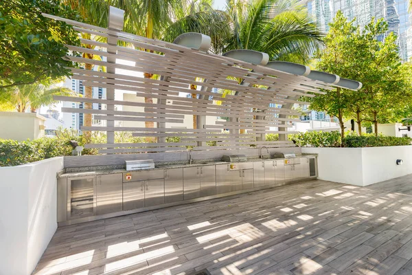 Beautiful outdoor kitchen, modern and elegant in stainless steel, surrounded by tropical vegetation, wooden floor, elegant design structure in the background