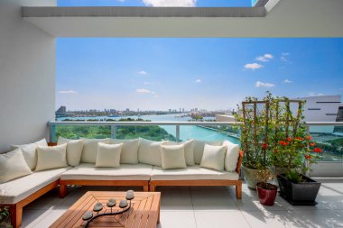 Beautiful terrace of a modern house, view from the balcony overlooking downtown Miami, outdoor armchair with cushions, coffee table, tropical plants, blue sky