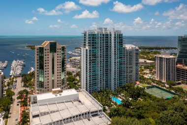 Aerial drone shot of Grovenor House Coconut Grove in Miami, abundant tropical vegetation around, modern buildings and towers, blue sky with clouds and city in the background