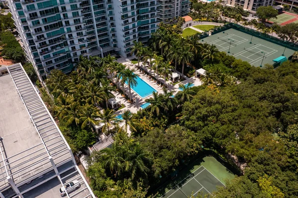 Aerial drone shot of Grovenor House Coconut Grove in Miami, abundant tropical vegetation around, modern buildings and towers, blue sky with clouds and city in the background