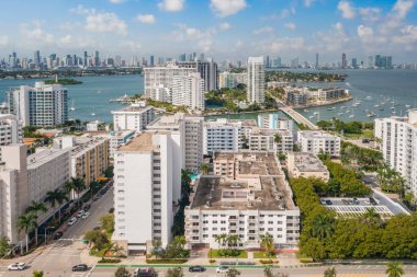 Aerial drone shot of the South Beach neighborhood in Miami, white buildings with balconies, condominiums, towers, modern city in the background, trees and palm trees around