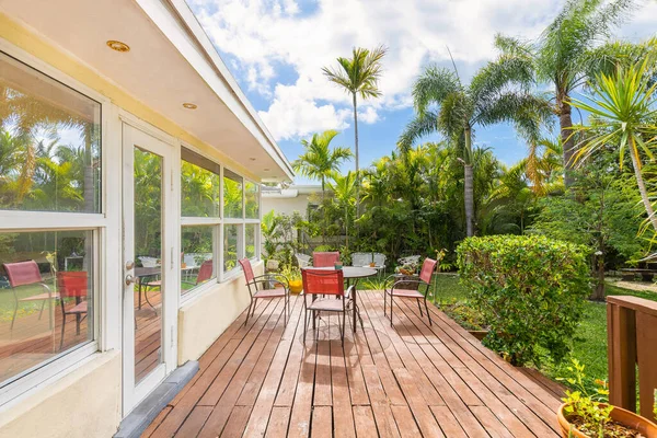 Beautiful backyard in the La Gorce neighborhood in Miami Beach, large tropical vegetation all around, outdoor furniture such as chairs and tables, wooden platform