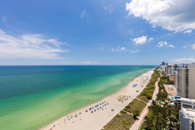 Miami Plajı 'ndaki Kuzey Sahili' nin insansız hava aracı görüntüsü, Akoya olarak bilinen bina, turkuaz deniz, şemsiyeler, modern binalar ve kuleler, mavi gökyüzü.