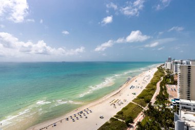 Miami Plajı 'ndaki Kuzey Sahili' nin insansız hava aracı görüntüsü, Akoya olarak bilinen bina, turkuaz deniz, şemsiyeler, modern binalar ve kuleler, mavi gökyüzü.
