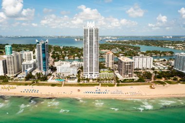 Miami Plajı 'ndaki Kuzey Sahili' nin insansız hava aracı görüntüsü, Akoya olarak bilinen bina, turkuaz deniz, şemsiyeler, modern binalar ve kuleler, mavi gökyüzü.