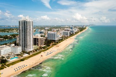 Miami Plajı 'ndaki Kuzey Sahili' nin insansız hava aracı görüntüsü, Akoya olarak bilinen bina, turkuaz deniz, şemsiyeler, modern binalar ve kuleler, mavi gökyüzü.