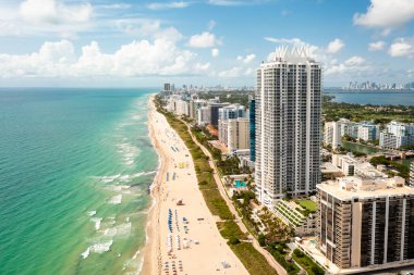 Miami Plajı 'ndaki Kuzey Sahili' nin insansız hava aracı görüntüsü, Akoya olarak bilinen bina, turkuaz deniz, şemsiyeler, modern binalar ve kuleler, mavi gökyüzü.