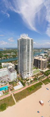 Miami Plajı 'ndaki Kuzey Sahili' nin insansız hava aracı görüntüsü, Akoya olarak bilinen bina, turkuaz deniz, şemsiyeler, modern binalar ve kuleler, mavi gökyüzü.