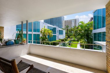 Bal Harbor villasındaki apartman balkonundan manzara, tropikal bitki örtüsü, kısa çimen, yaz havası, beyaz duvarlar, yol girişleri, kahverengi taş ayrıntılar, turkuaz pencereler