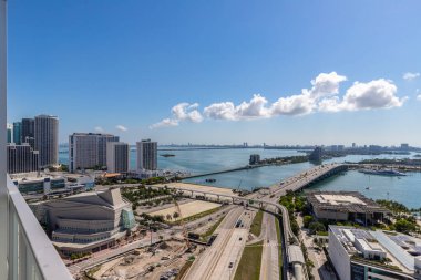 Miami şehir merkezindeki ticari alanın arkasından havadan çekilen görüntüler parklar, köprüler, arabalar, kahverengi binalar, müzeler, kuleler, rıhtımlar ve mavi gökyüzü.