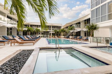 Miami şehir merkezinin avlu manzarası, kaplıcalı havuz, bolca şezlong, havuz, spa ve jakuzi, palmiye, şemsiye ve mavi gökyüzü.