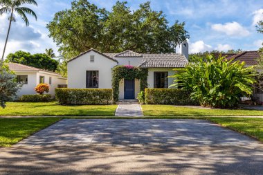 Sömürge tarzı ve modern beyaz evin önünde, Miami-Dade 'in Miami sahilinde, kapıda özel kemerli, özel bir yol, kaldırım, kısa çimenler, fayanslı çatı, ağaçlar ve palmiyeler, arka planda mavi gökyüzü.