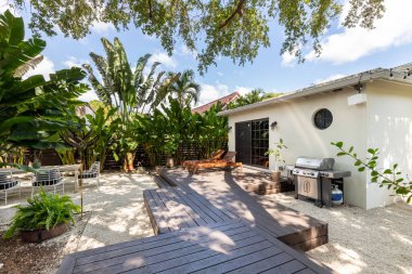 Miami, ABD 'de modern tarz evlerin güzel bir avlusu var. Verandayı geçen yüzen ahşap zemin, açık hava gaz ızgarası, ağaçlar, taş patika, güneş pansiyonları, tropikal bitkiler.