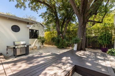 Miami, ABD 'de modern tarz evlerin güzel bir avlusu var. Verandayı geçen yüzen ahşap zemin, açık hava gaz ızgarası, ağaçlar, taş patika, güneş pansiyonları, tropikal bitkiler.