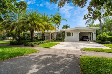ABD 'nin Miami-Dade şehrindeki Coral Gables şehrinde modern ve lüks bir koloni tarzı evin ön cephesinde geniş bir tropikal bitki örtüsü, açık garaj, ana giriş, kaldırım, kısa çimen, özel çiçek yatakları