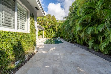 Beton zemin ve havuzu olan güzel bir bahçe, tropikal bitkilerle çevrili, güneşli verandalı, açık mobilyalı, sarmaşıklı, Coral Gables 'da yer alan