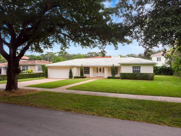 Beautiful front of a modern and elegant house in the Golden Triangle neighborhood in the city of Coral Gables, short grass, tropical vegetation around, blue sky