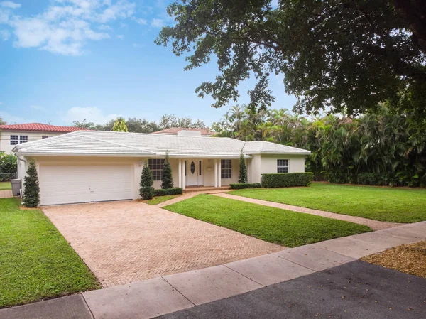 Beautiful front of a modern and elegant house in the Golden Triangle neighborhood in the city of Coral Gables, short grass, tropical vegetation around, blue sky