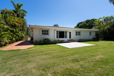 ABD 'nin Miami-Dade şehrindeki Coral Gables şehrinde modern ve lüks bir koloni tarzı evin ön cephesinde geniş bir tropikal bitki örtüsü, açık garaj, ana giriş, kaldırım, kısa çimen, özel çiçek yatakları
