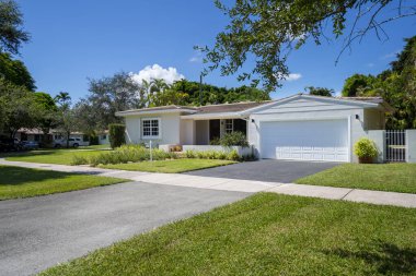 ABD 'nin Miami-Dade şehrindeki Coral Gables şehrinde modern ve lüks bir koloni tarzı evin ön cephesinde geniş bir tropikal bitki örtüsü, açık garaj, ana giriş, kaldırım, kısa çimen, özel çiçek yatakları