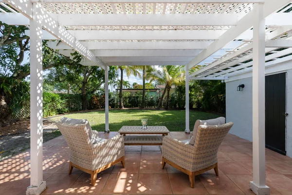 Beautiful patio with a wooden shed, with armchairs and an outdoor table in the West Flagler neighborhood, in Little Havana, short grass, privet walls, trees and palm trees, light blue walls and blue sky