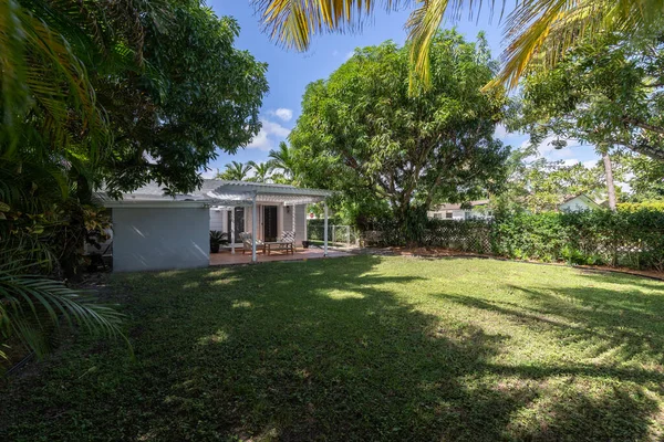 Beautiful patio with a wooden shed, with armchairs and an outdoor table in the West Flagler neighborhood, in Little Havana, short grass, privet walls, trees and palm trees, light blue walls and blue sky