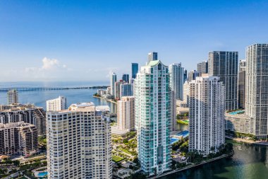 Brickell Key bölgesinin insansız hava aracı görüntüleri, bir sürü kule ve modern binalar, ticari şehir manzarası, deniz ve kanallarla çevrili, yelkenliler, rıhtımlar, köprüler, caddeler, mavi gökyüzü ve turkuaz deniz.