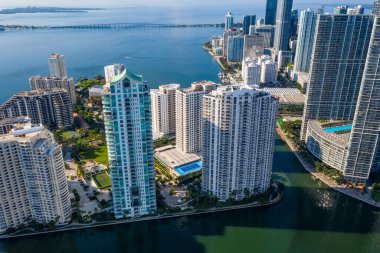 Brickell Key bölgesinin insansız hava aracı görüntüleri, bir sürü kule ve modern binalar, ticari şehir manzarası, deniz ve kanallarla çevrili, yelkenliler, rıhtımlar, köprüler, caddeler, mavi gökyüzü ve turkuaz deniz.