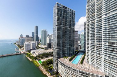 Brickell Key bölgesinin insansız hava aracı görüntüleri, bir sürü kule ve modern binalar, ticari şehir manzarası, deniz ve kanallarla çevrili, yelkenliler, rıhtımlar, köprüler, caddeler, mavi gökyüzü ve turkuaz deniz.